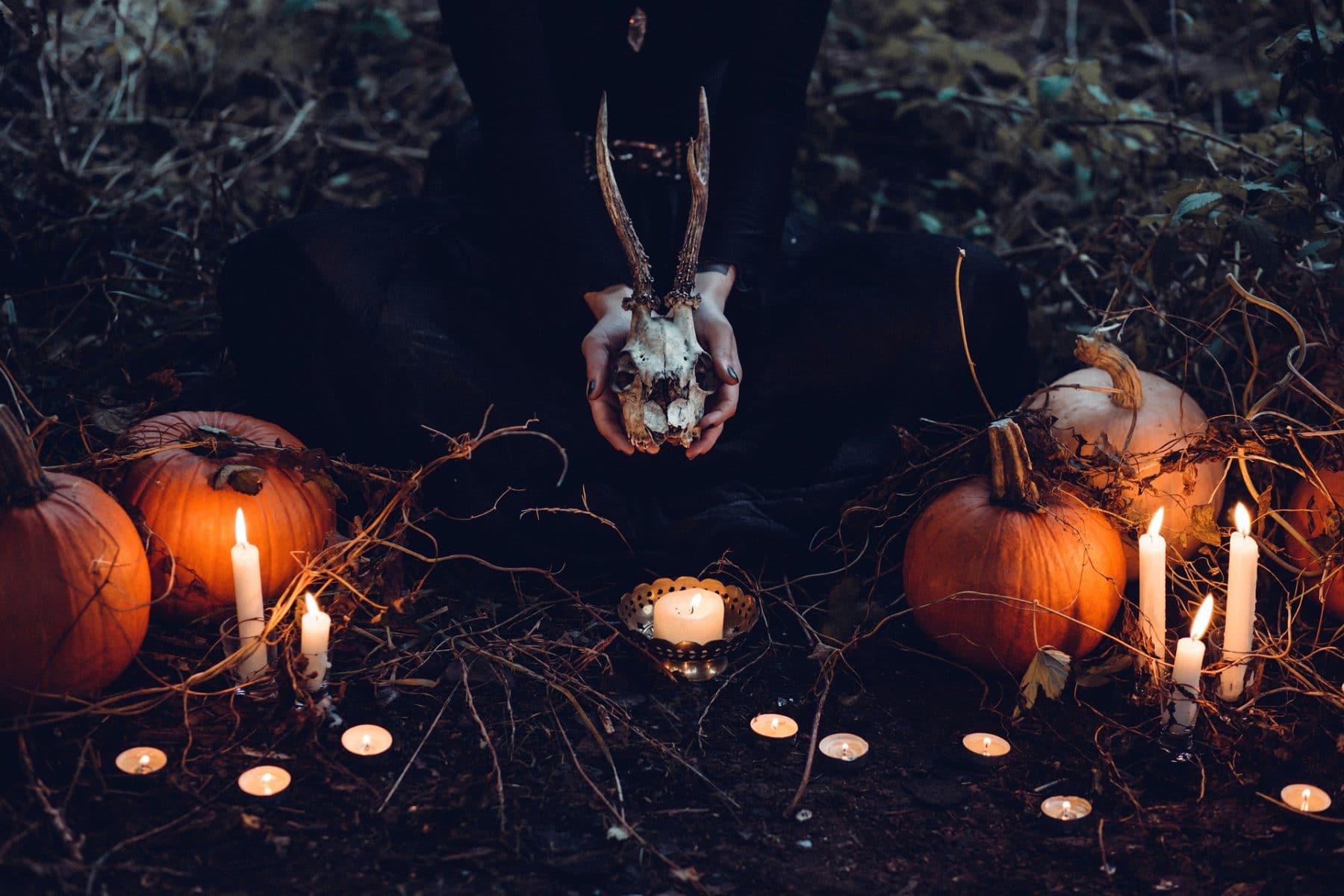 image of woman surrounded by pumpkins and candles, holding a skull